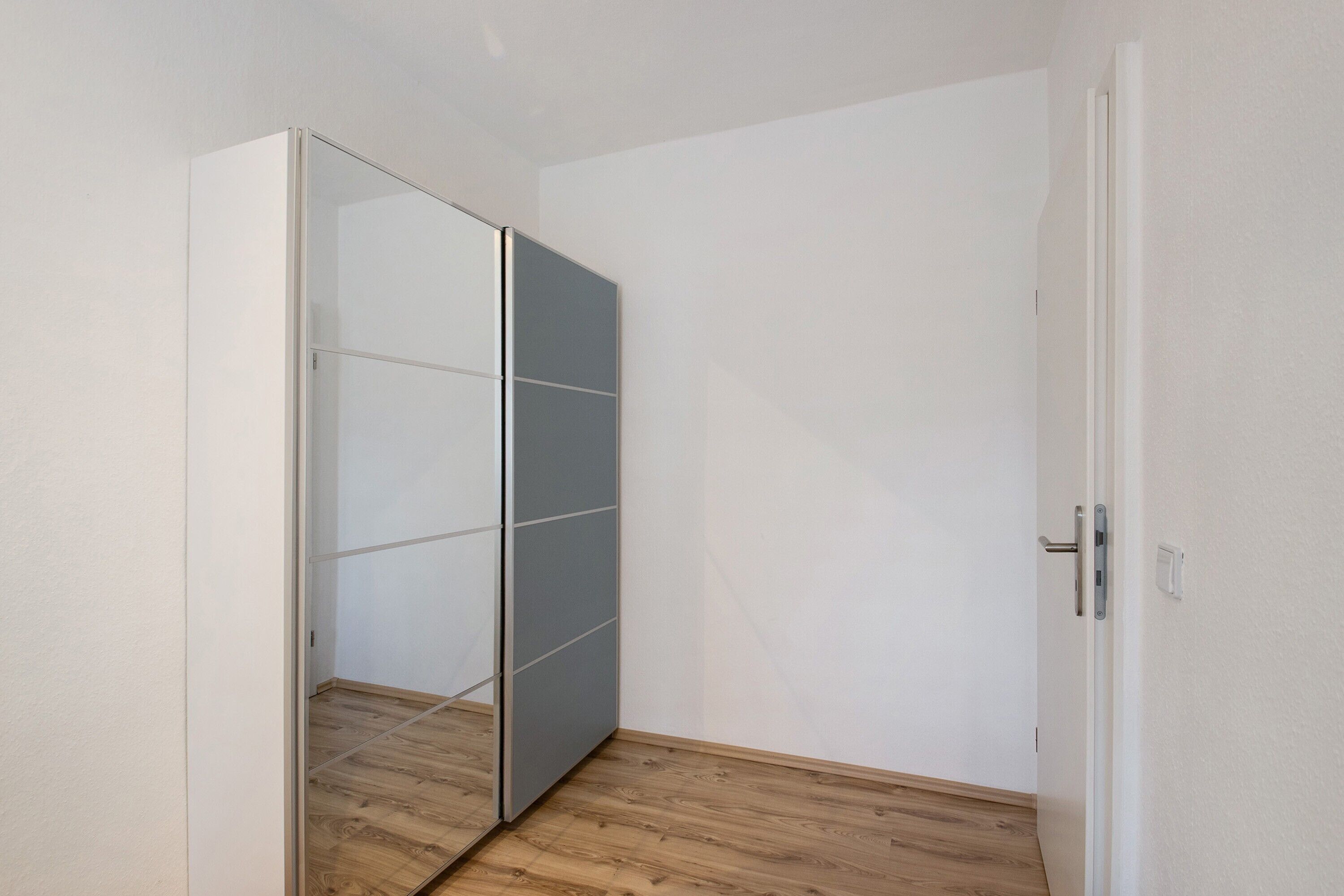 A room with a wooden floor, a white door, and a grey sliding closet.
