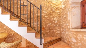 Una escalera con barandillas ornamentadas y escalones estampados, que conduce a una habitación con paredes de piedra y un armario de madera.