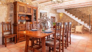 Un comedor con una mesa y sillas de madera, un armario con cristalería, y una escalera al fondo.