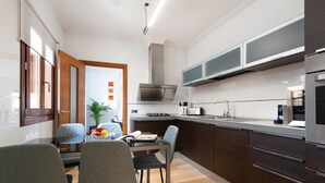 A modern kitchen with dark cabinetry, a stainless steel range hood, and a built-in oven. There is a dining area with a table and chairs, and a small plant on the windowsill. - Can Joan (maria) - Apartment With Private Pool (, Illes Balears)