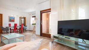 A modern living room with a flat-screen TV, glass coffee table, and a dining area with red chairs. - Can Joan (maria) - Apartment With Private Pool (, Illes Balears)