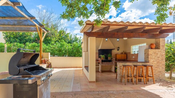 An outdoor kitchen area with a grill, bar stools, and a pergola. - Es Garroveret - Villa With Private Pool. Free Wifi (, Illes Balears)