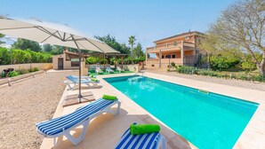 A swimming pool with lounge chairs and umbrellas, surrounded by a landscaped garden and a building with a balcony. - Es Garroveret - Villa With Private Pool. Free Wifi (, Illes Balears)