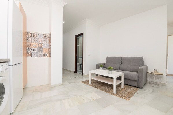 Una sala de estar moderna con un sofá gris, una mesa de centro blanca y una lavadora en una esquina.