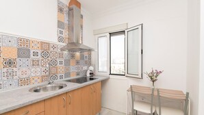 A kitchen with patterned tiles, a stainless steel sink, wooden cabinets, and a small dining area with a table and chairs.