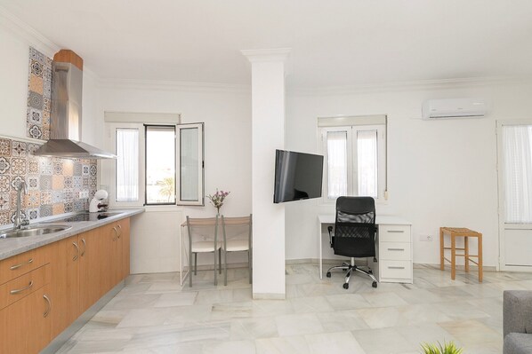 Una cocina moderna con estufa integrada, una zona de comedor con mesa y sillas, una silla de oficina negra y un taburete de madera pequeño.