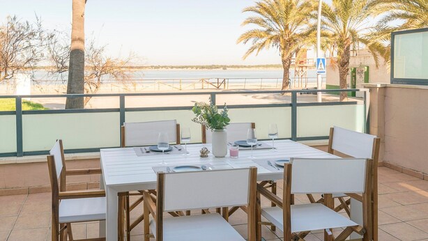 A dining area with a table set for four, overlooking a beach.