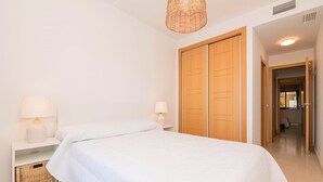 A bedroom with a bed, two bedside tables with lamps, a wicker basket, and a wooden wardrobe.