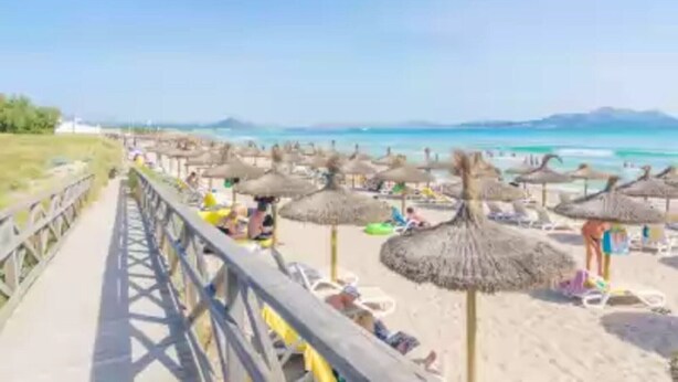 Une plage avec des parasols en chaume et des chaises longues, une promenade en bois et une vue dégagée sur l’océan.