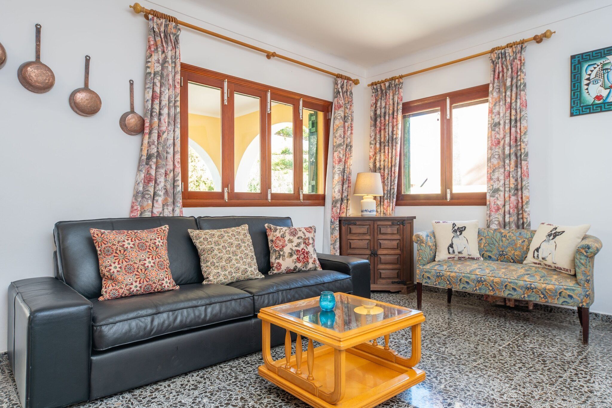 A living room with a black leather sofa, a wooden coffee table, and a patterned sofa.
