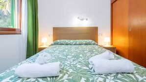 A hotel room with a bed, two bedside lamps, a nightstand, a wooden wardrobe, and a window with curtains.