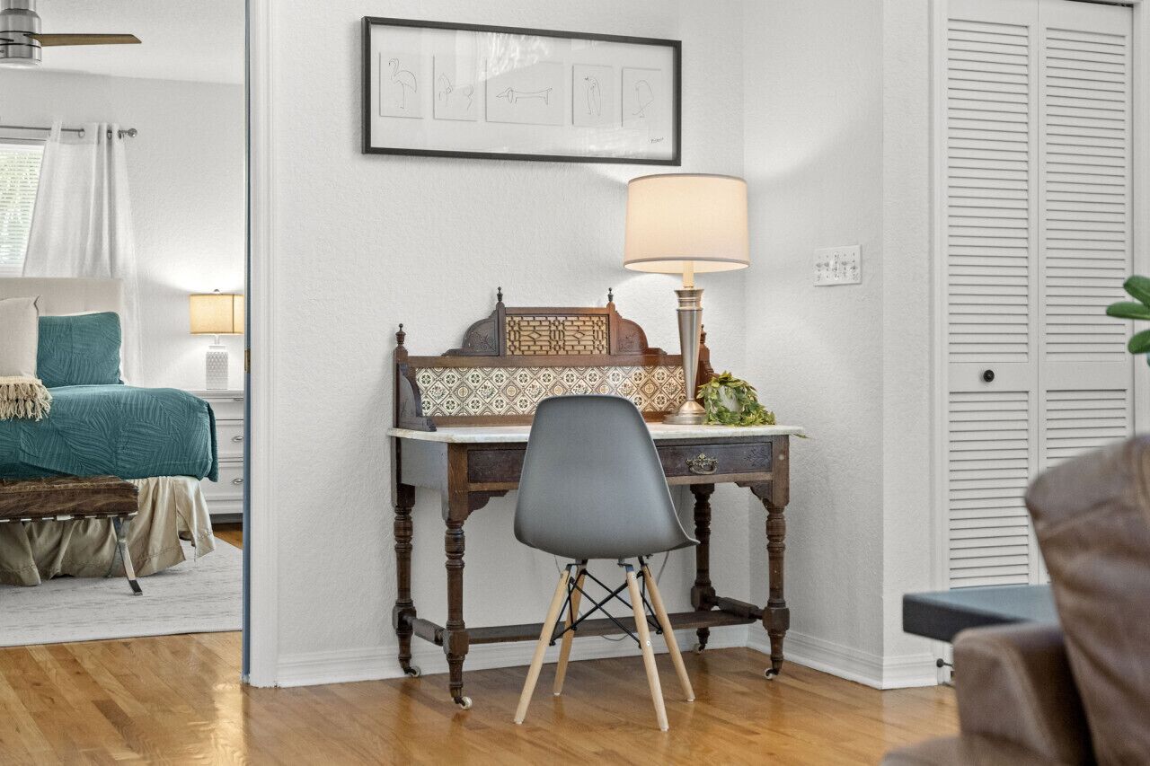 A bedroom with a bed, bedside table, lamp, and a desk with a chair.