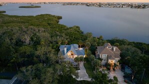 A large house with a driveway and a swimming pool, surrounded by trees and a body of water. - Mangrove Manor | Waterfront + Backyard Oasis (Seminole)