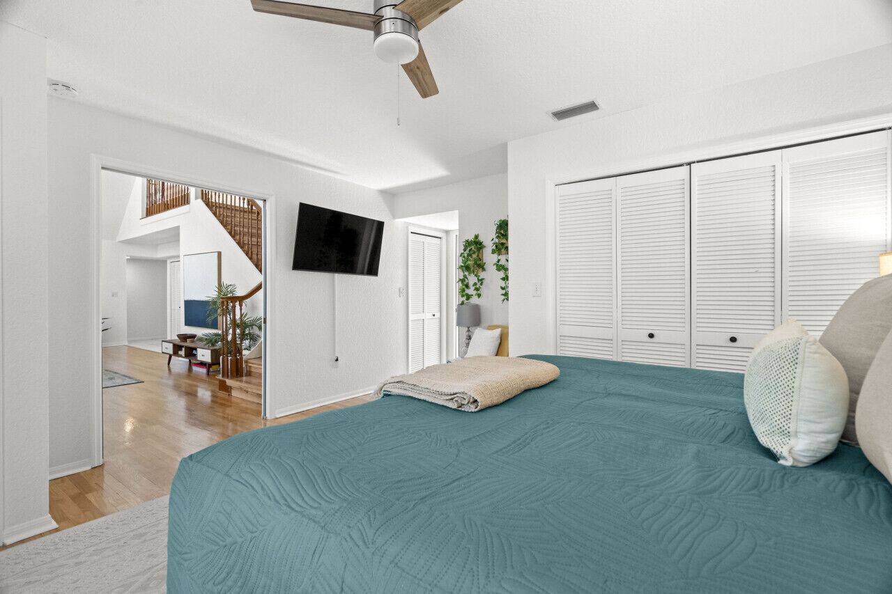 A bedroom with a bed, a ceiling fan, a TV, and a closet.
