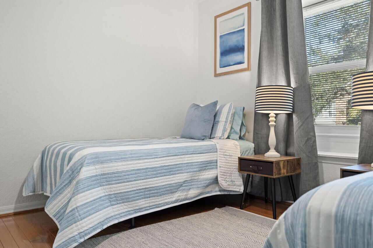 Een slaapkamer met een bed, nachtkastje, lamp en een raam met gordijnen.