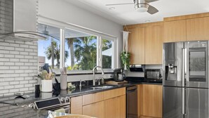 A modern kitchen with a stainless steel refrigerator, a built-in oven, and a large window overlooking a tropical landscape. - Mangrove Manor | Waterfront + Backyard Oasis (Seminole)