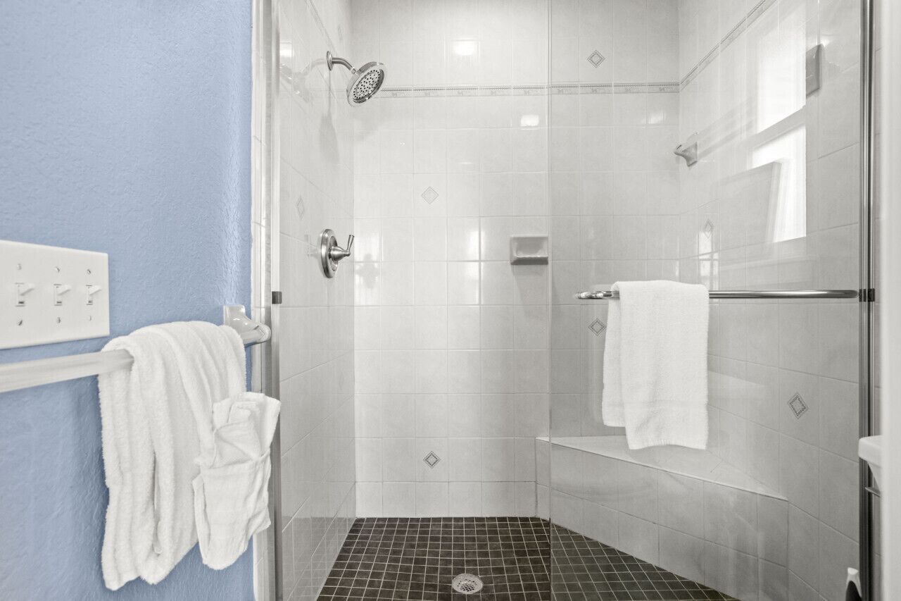 Eine barrierefreie Dusche mit Glastür, weiß geflieste Wände und einer blauen Akzentwand.