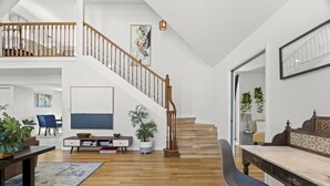 A spacious living area with a wooden staircase, a dining table, and a blue chair. - Mangrove Manor | Waterfront + Backyard Oasis (Seminole)