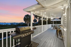 Une terrasse extérieure couverte, équipée d’un barbecue, de tables et de chaises, et offrant une vue sur une étendue d’eau.