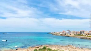 Une ville côtière avec des bâtiments qui bordent la plage, une eau d’un bleu limpide et un paysage rocheux au premier plan.