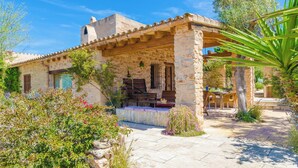 Un bâtiment en pierre doté d’un patio couvert, d’un espace extérieur aménagé et d’une végétation luxuriante.