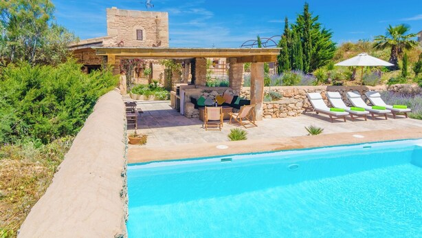 Un espace piscine avec des chaises longues, une pergola et un bâtiment en pierre en arrière-plan.