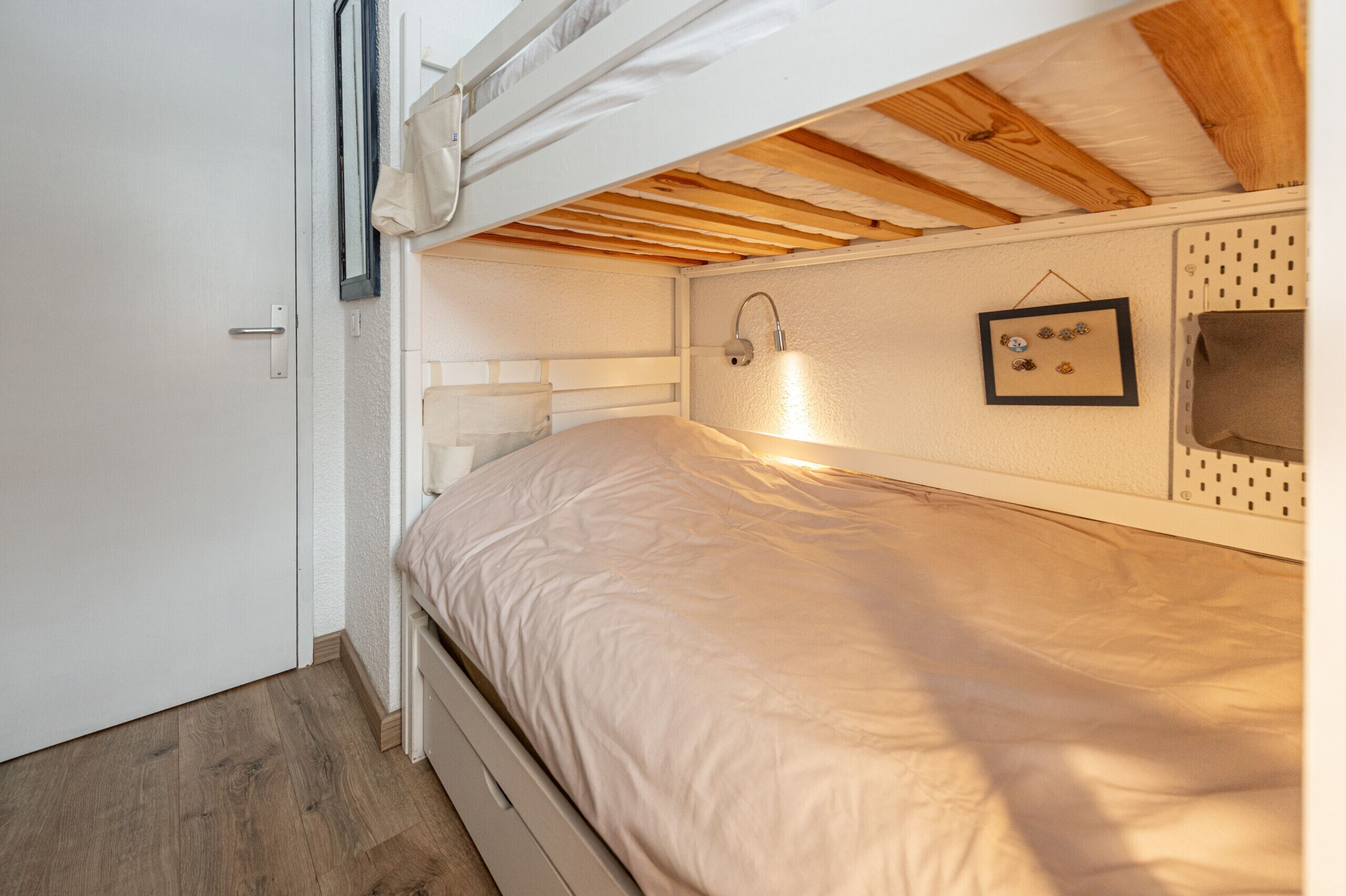 Ein Stockbett mit Kopfteil, einer Nachttischlampe und einem Wandregal mit Dekoration.