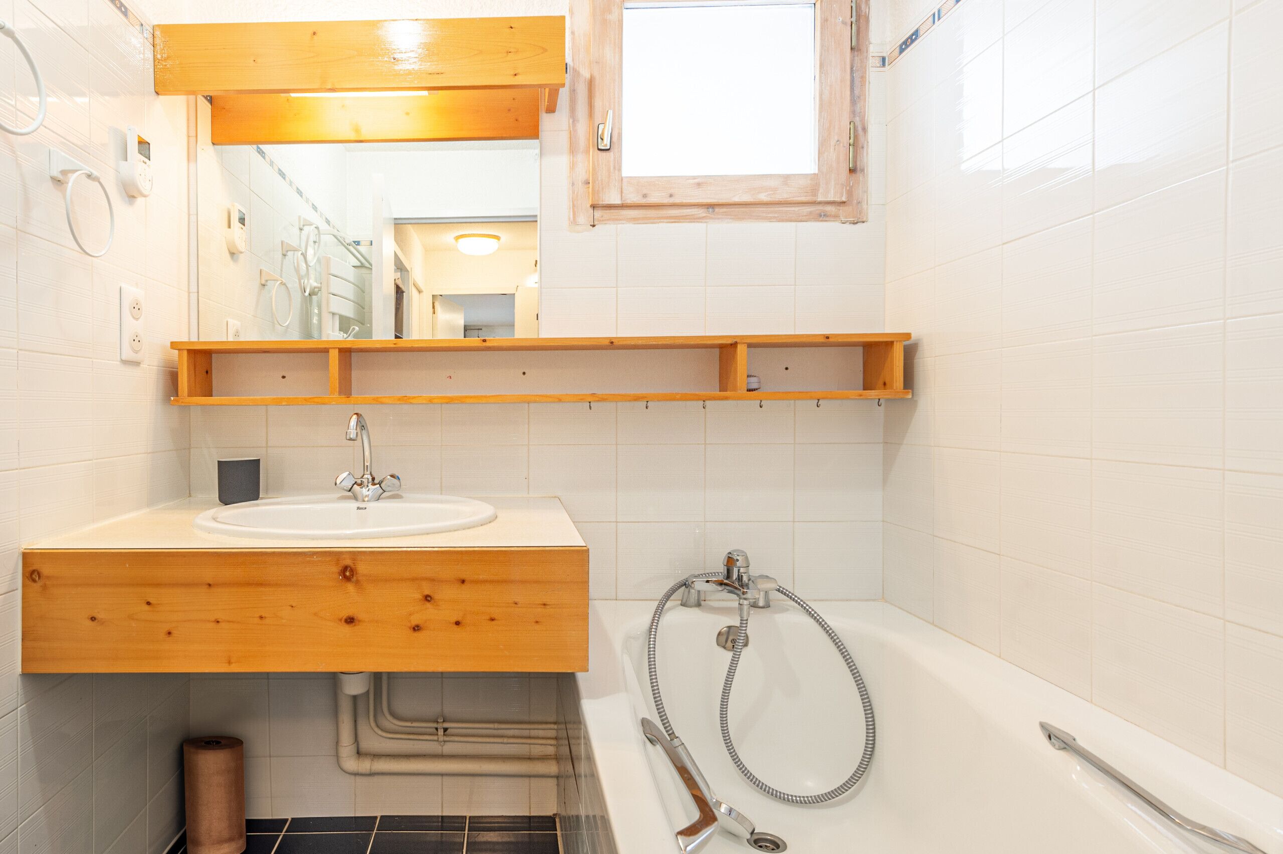 Une salle de bain avec un meuble-lavabo en bois, un évier, un miroir, une douche et une fenêtre.