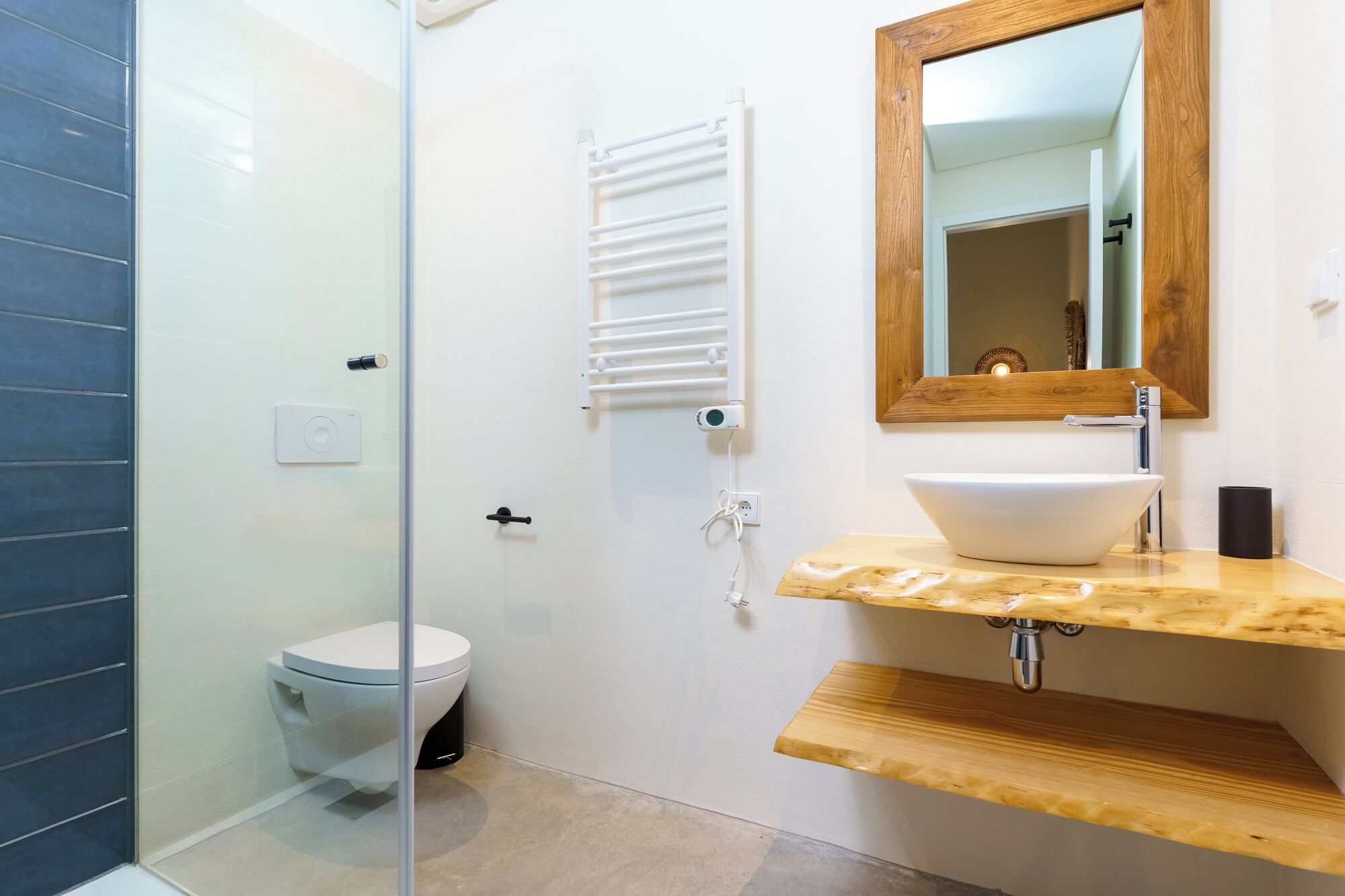 A modern bathroom with a glass shower enclosure, a white toilet, a wooden vanity with a white sink, and a mirror with a wooden frame.