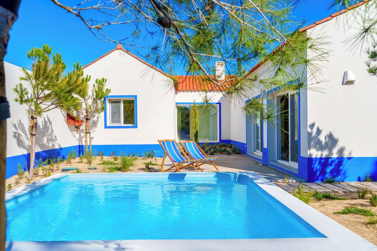 Ett modernt hus med en swimmingpool, två solstolar och en klarblå himmel.