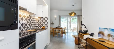 Una cucina moderna con forno a microonde, forno e zoccolo decorato. C'è una zona pranzo con tavolo e sedie, e vista all'esterno tramite una porta vetrata.
