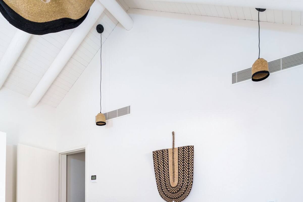Ett sovrum med en säng, en hängande lampa, en dekorativ detalj som hänger på väggen och ett nattduksbord i trä.
