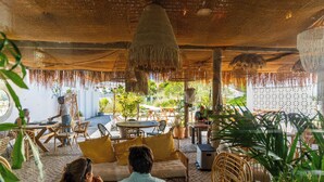 An outdoor seating area with wicker furniture, hanging baskets, and a thatched ceiling. - La Réserve Comporta (Grandola)