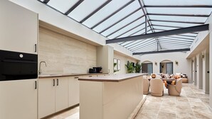 A modern kitchen with a central island, a dining area with chairs, and a glass ceiling.