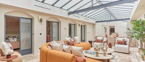 A spacious living area with a high ceiling and skylight, featuring a large orange sofa, multiple seating options, and a well-lit environment.