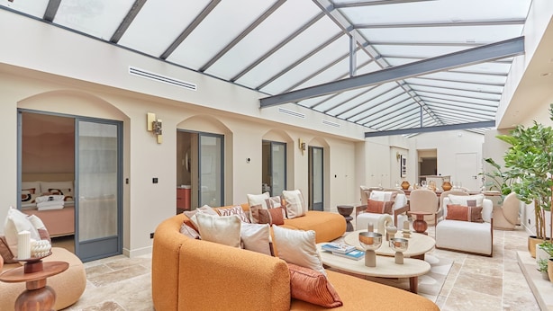 A spacious living area with a high ceiling and skylight, featuring a large orange sofa, multiple seating options, and a well-lit environment.