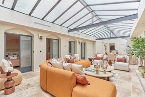 Un amplio salón con techo alto y tragaluces, que incluye un sofá naranja grande, diversas opciones de asientos y un ambiente bien iluminado.