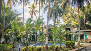 A resort with multiple bungalow-style buildings surrounded by palm trees and a swimming pool. - La Perla Resort By Circle Hotels&Resort (Morjim)