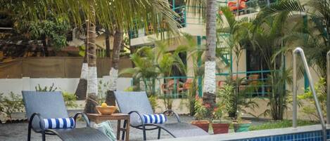 A poolside area with two lounge chairs, a small table, and potted plants.