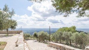 Eine Steintreppe führt zu einer Aussichtsplattform mit Blick auf eine Landschaft, Bäume und eine entfernte Meeresansicht.