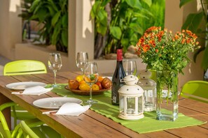 A wooden dining table set with plates, glasses, a bottle of wine, a bowl of fruit, and a vase with flowers.