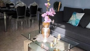 Una sala de estar moderna con una mesa de centro de vidrio, sillas traslúcidas, un sofá y un cuadro en la pared.