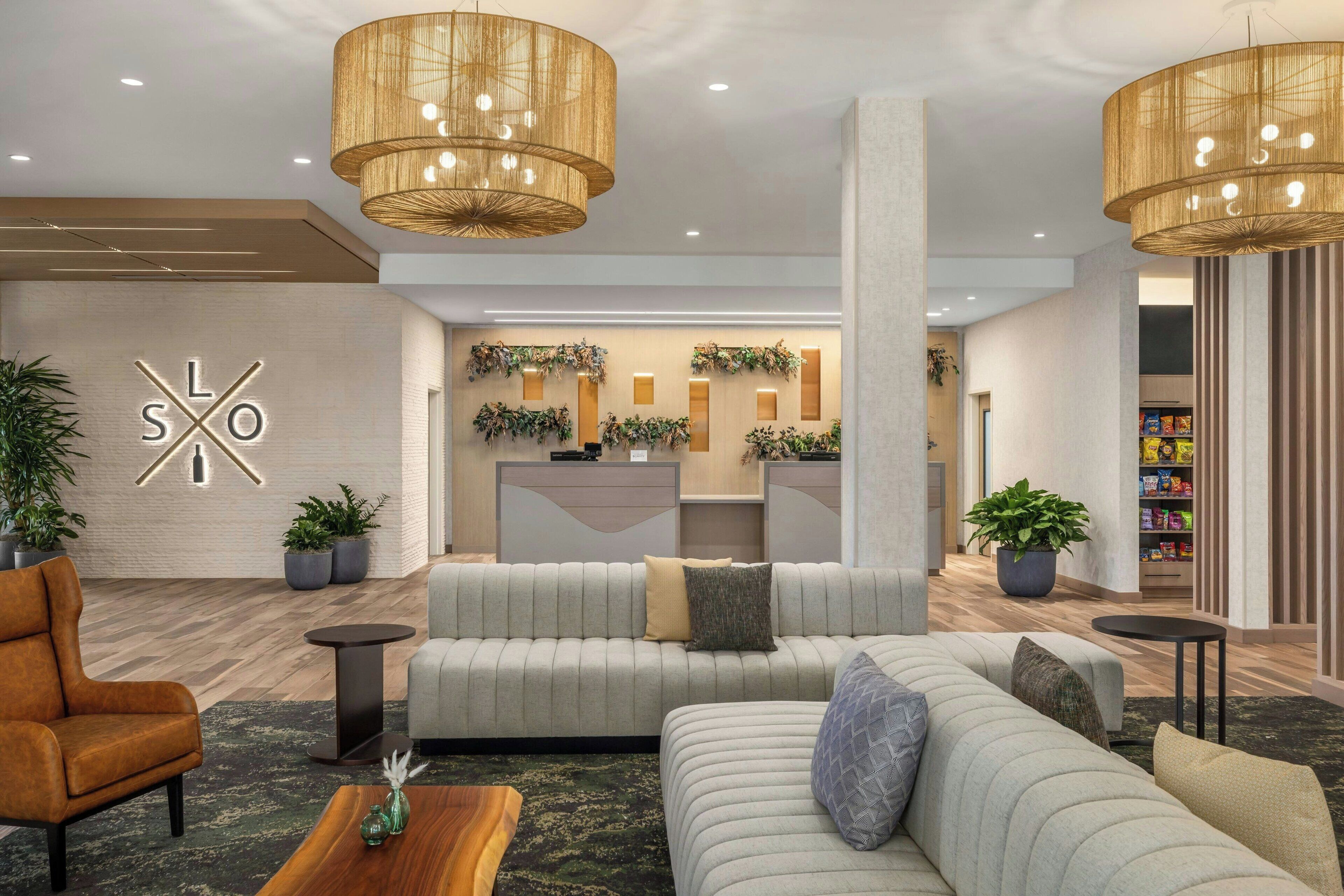 A modern lobby with a reception desk, sofas, and potted plants.