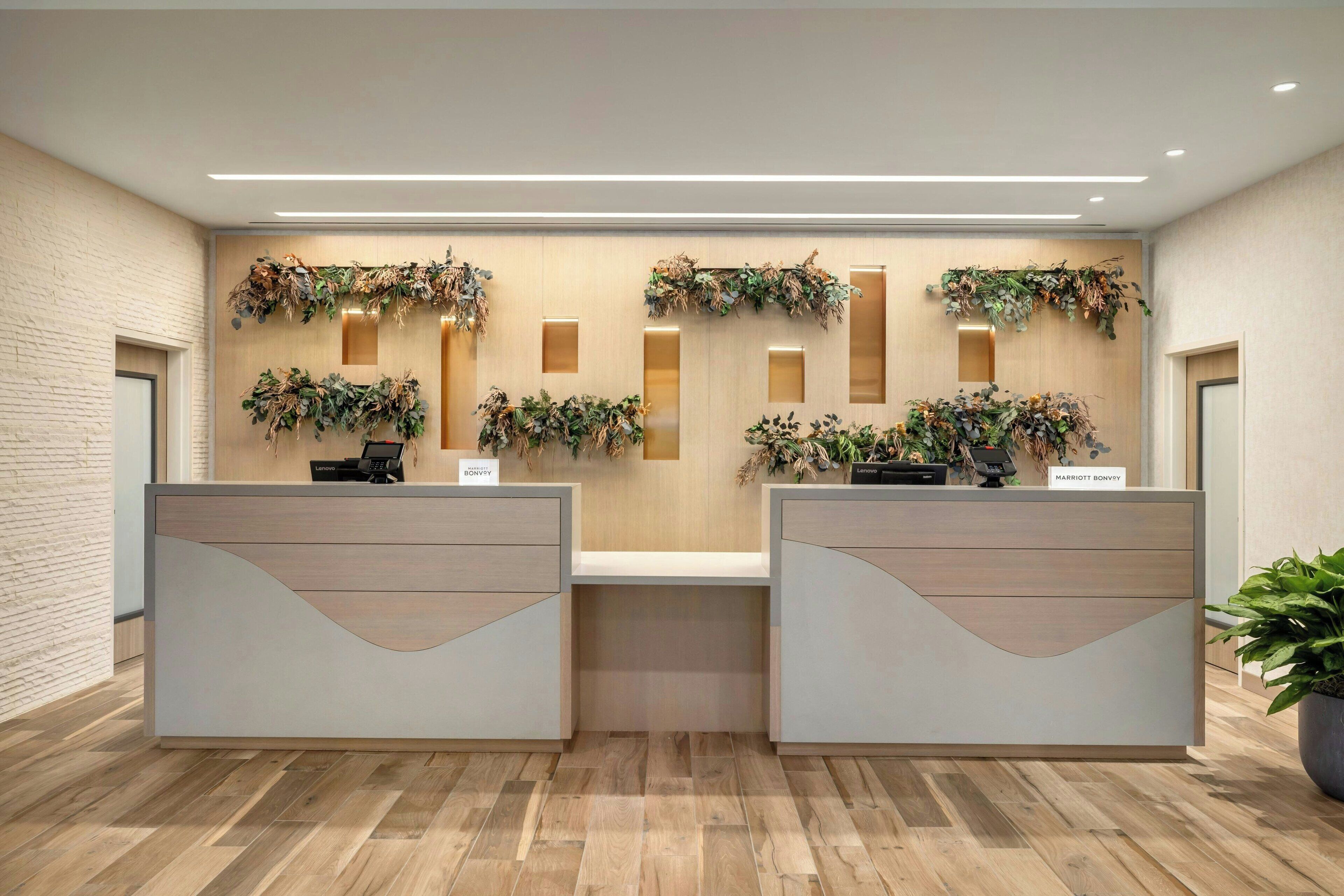 Een receptiebalie met twee toonbanken, elk met een naam erop, en een houten wand met verticale plantenopstellingen.