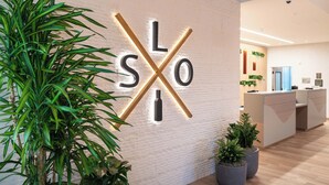 Un mostrador de recepción de diseño moderno, un cartel con letras iluminadas en la pared y plantas en macetas.
