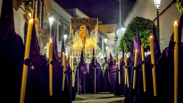Eine Prozession von Personen in violetten Roben mit Kerzen, die zu einem geschmückten Altar führt.