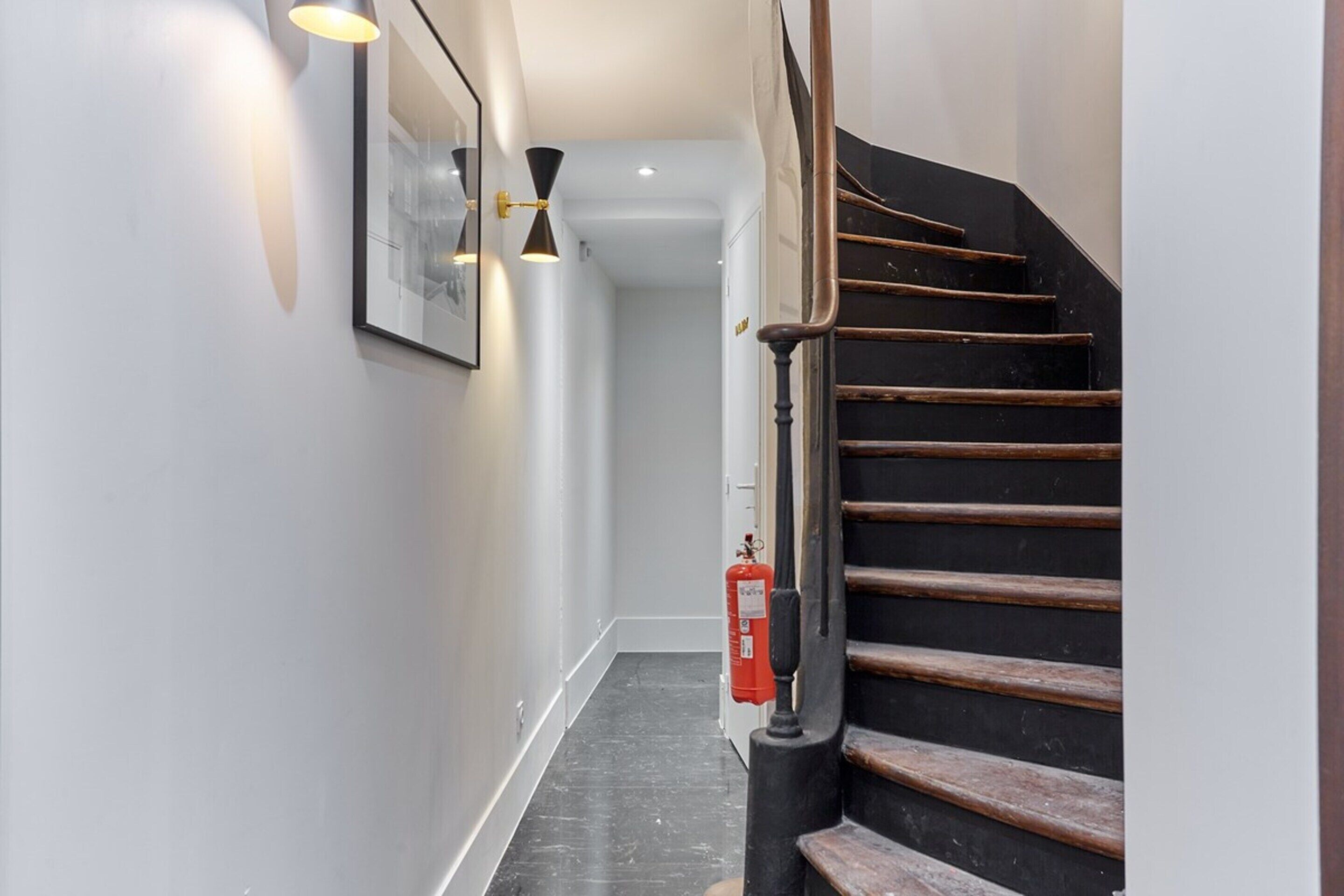 A modern staircase with wooden steps and a black handrail, leading to an upper floor.
