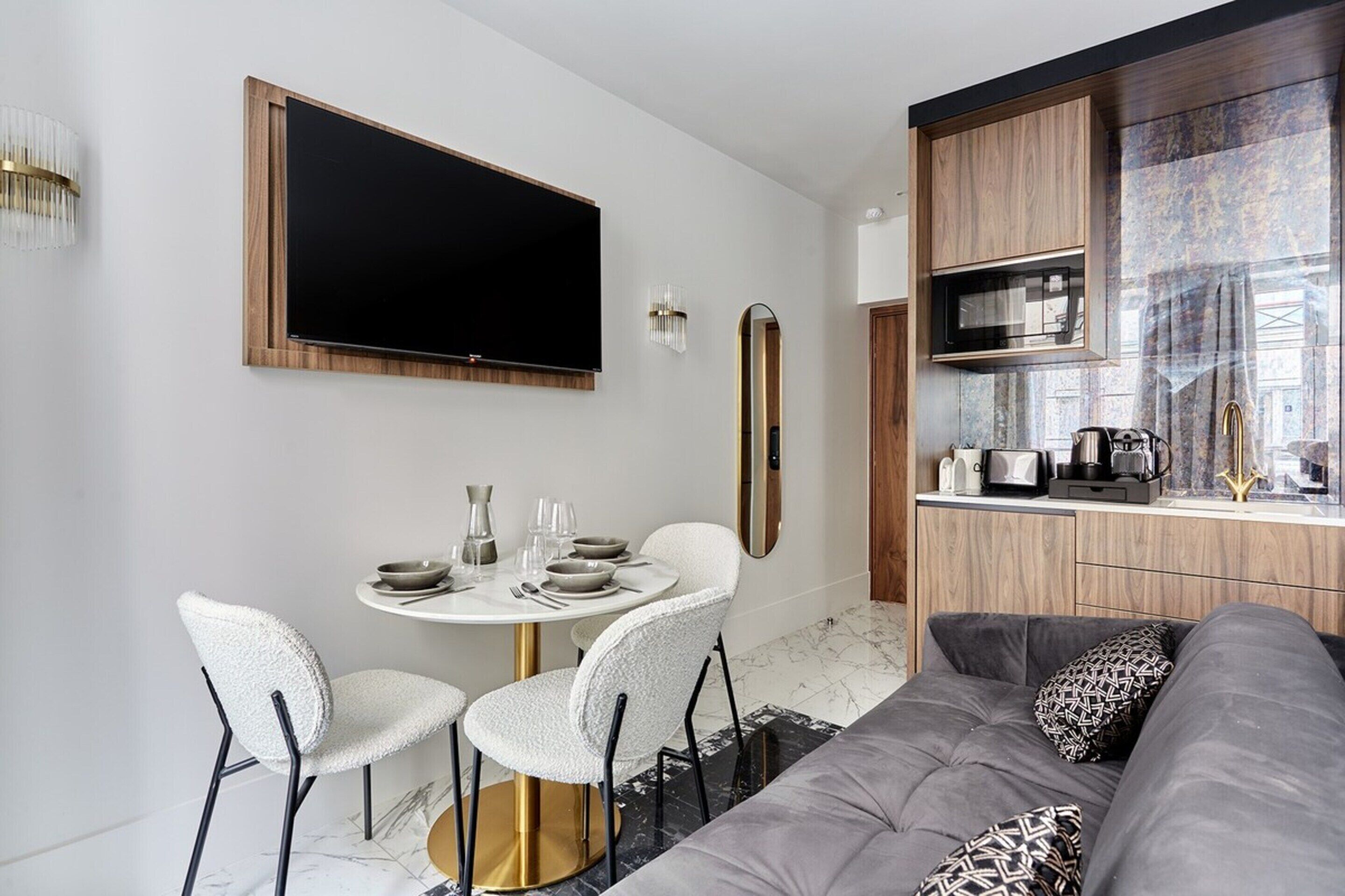 A modern living space with a dining area, a sofa, a TV, and a kitchen area.