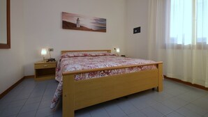 Ett sovrum med en säng i trä, två sängbord med lampor, en tavla på väggen och ett fönster med gardiner.