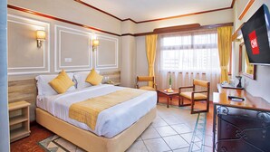 Une chambre d’hôtel avec un grand lit, des tables de chevet, un bureau avec une chaise, une télévision et une fenêtre avec des rideaux.